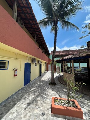 A courtyard with a tiled floor, a palm tree, and a covered seating area. - Villa Di Verona (Guarujá)