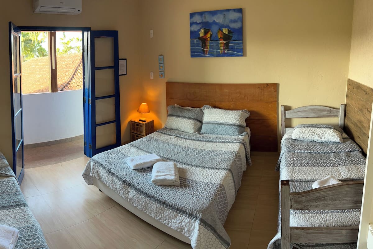 A hotel room with a large bed, two smaller beds, a wooden headboard, a painting on the wall, and a door leading outside.