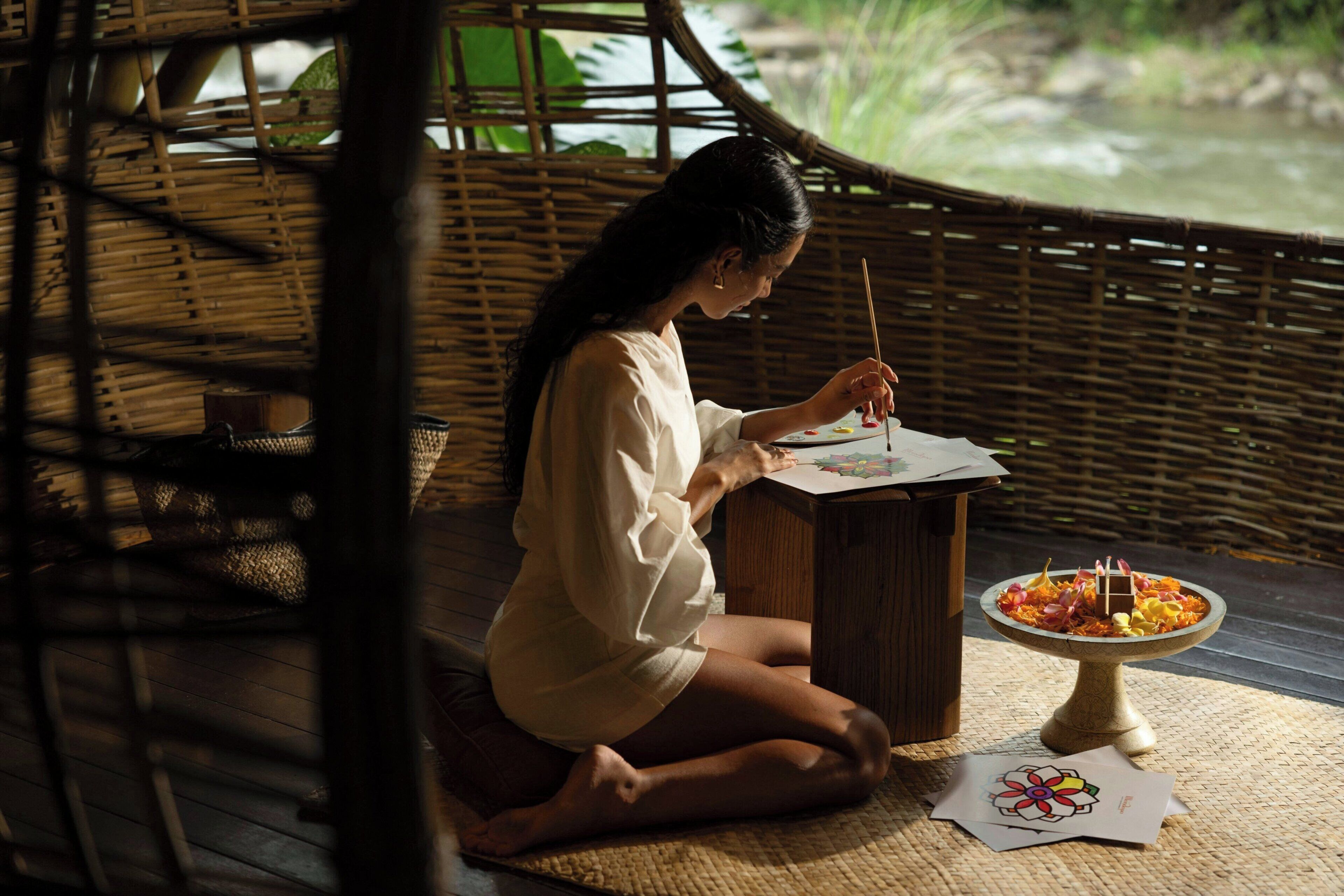 A person sitting on a mat, painting a picture.