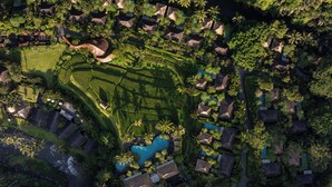 Vue aérienne d’un complexe hôtelier avec des bungalows aux toits de chaume, une piscine centrale et une végétation luxuriante.