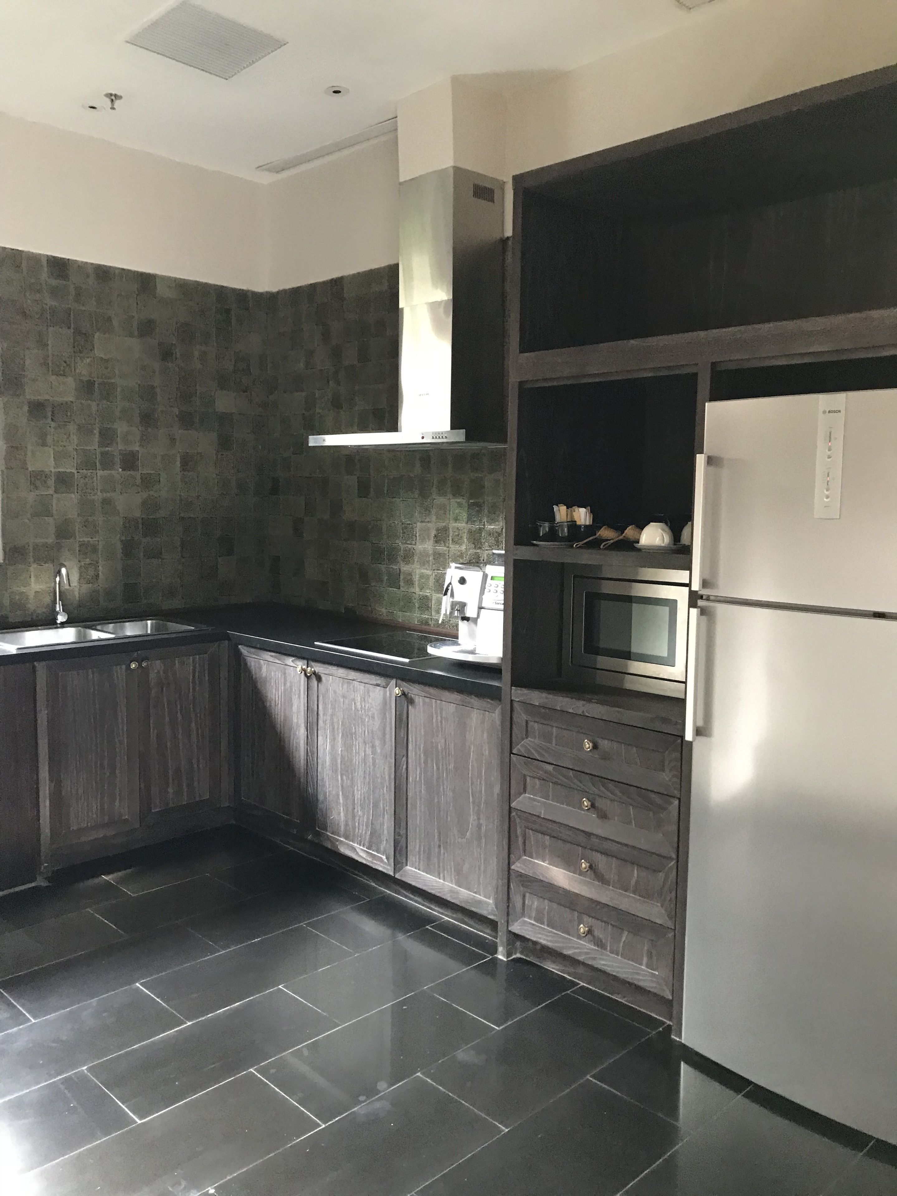 A modern kitchen with dark wooden cabinets, a stainless steel sink, a Bosch refrigerator, and a built-in oven.