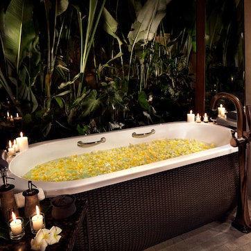Una bañera llena de flores amarillas, rodeada de velas y plantas.
