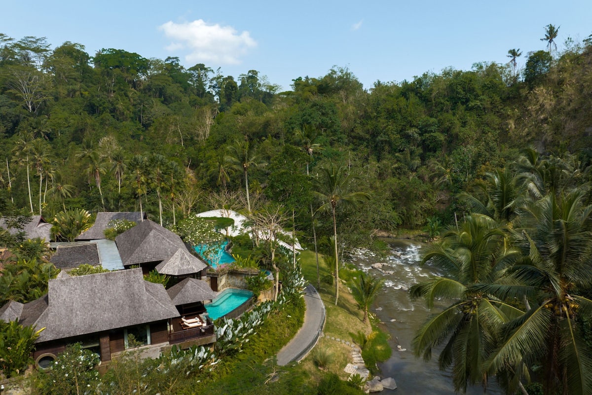 A resort with multiple thatched-roof buildings, a swimming pool, and a river running through the property.