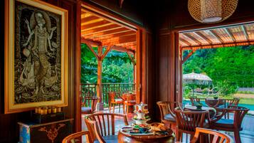A restaurant with wooden furniture, a large framed artwork, and a view of lush greenery.