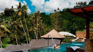 Un espace piscine agrémenté de chaises longues, d’une structure à toit de chaume et d’une végétation tropicale luxuriante.