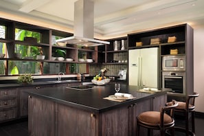 A modern kitchen with a large central island, dark wood cabinetry, and built-in appliances including a microwave and oven.