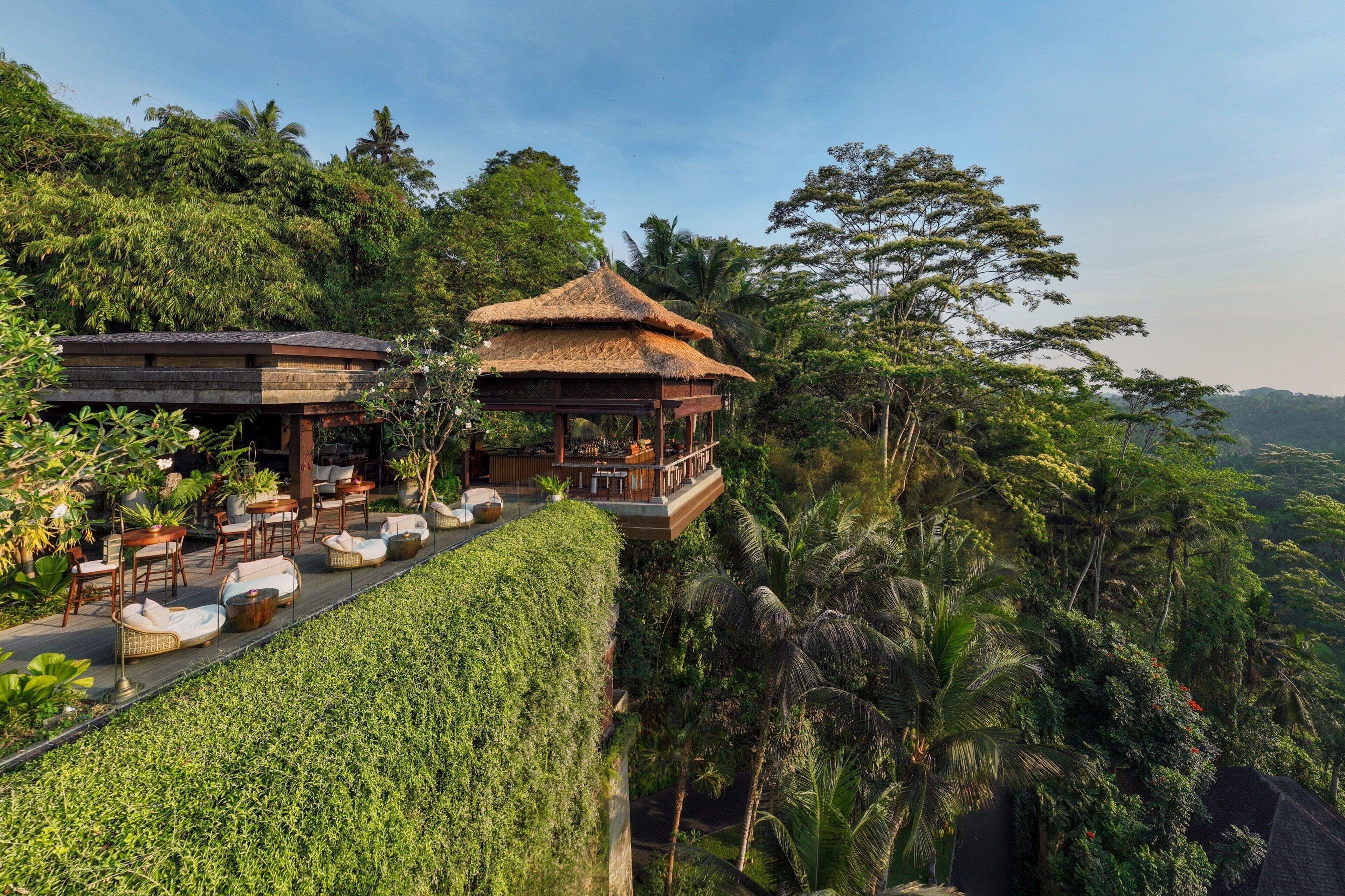 A luxurious outdoor lounge area with a thatched-roof gazebo, surrounded by lush greenery and a well-maintained hedge.