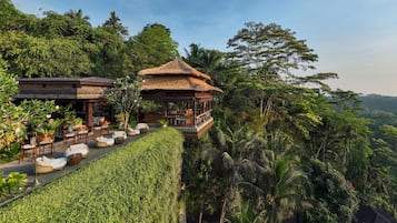 Un espace de détente extérieur luxueux, doté d’un belvédère à toit de chaume, entouré d’une végétation luxuriante et d’une haie bien entretenue.