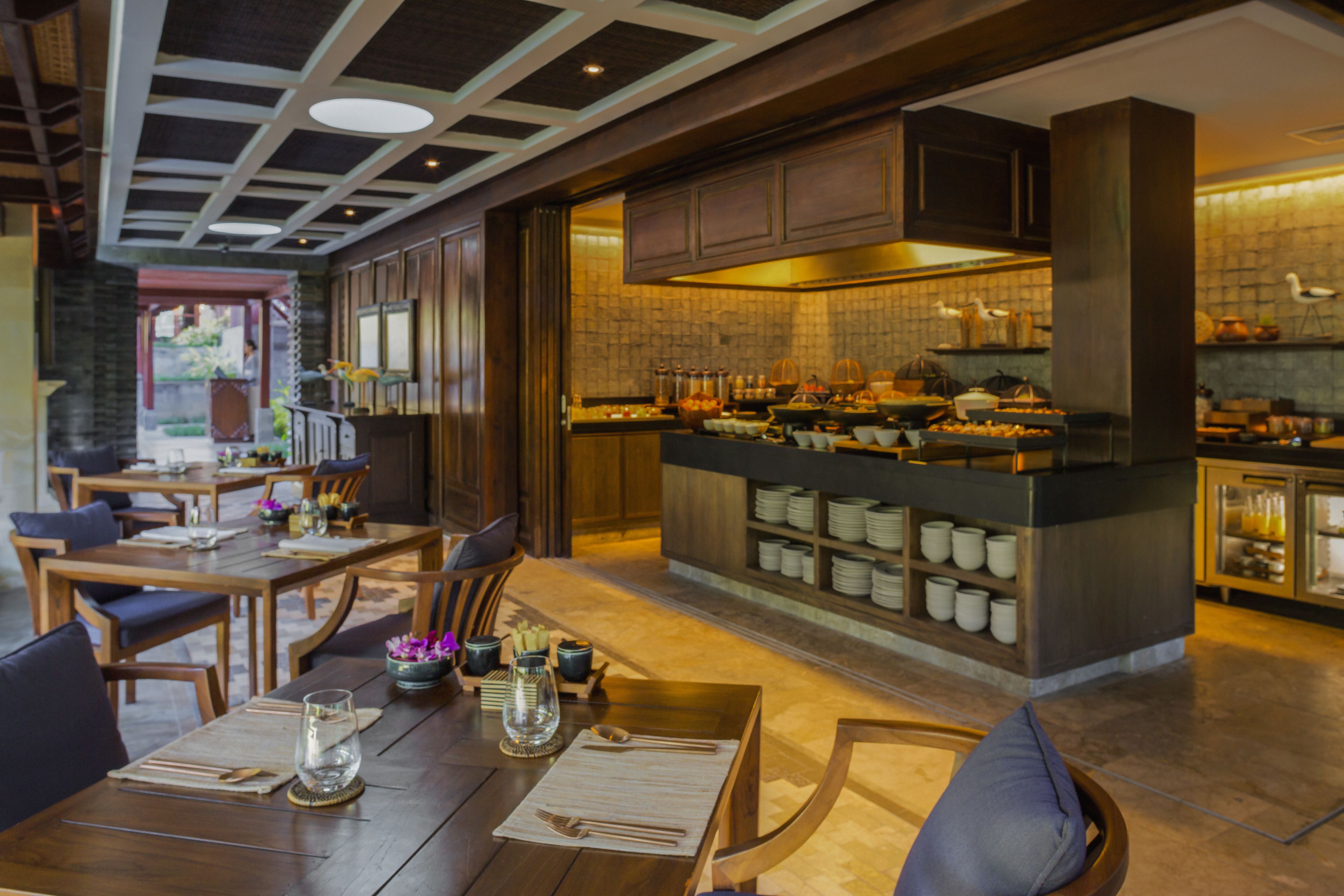 Un restaurant doté de meubles en bois, d’un bar et d’une cuisine visible à travers une porte ouverte.