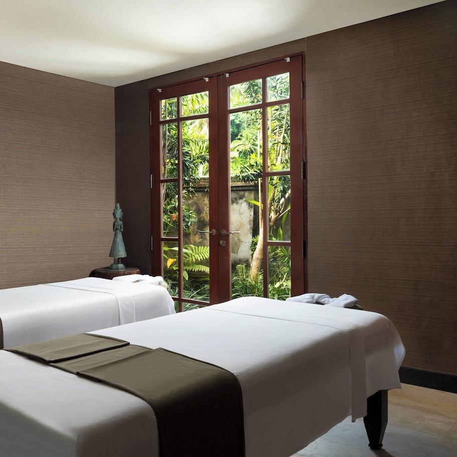 A room with two beds, a window with a view of greenery, and a statue on a table.