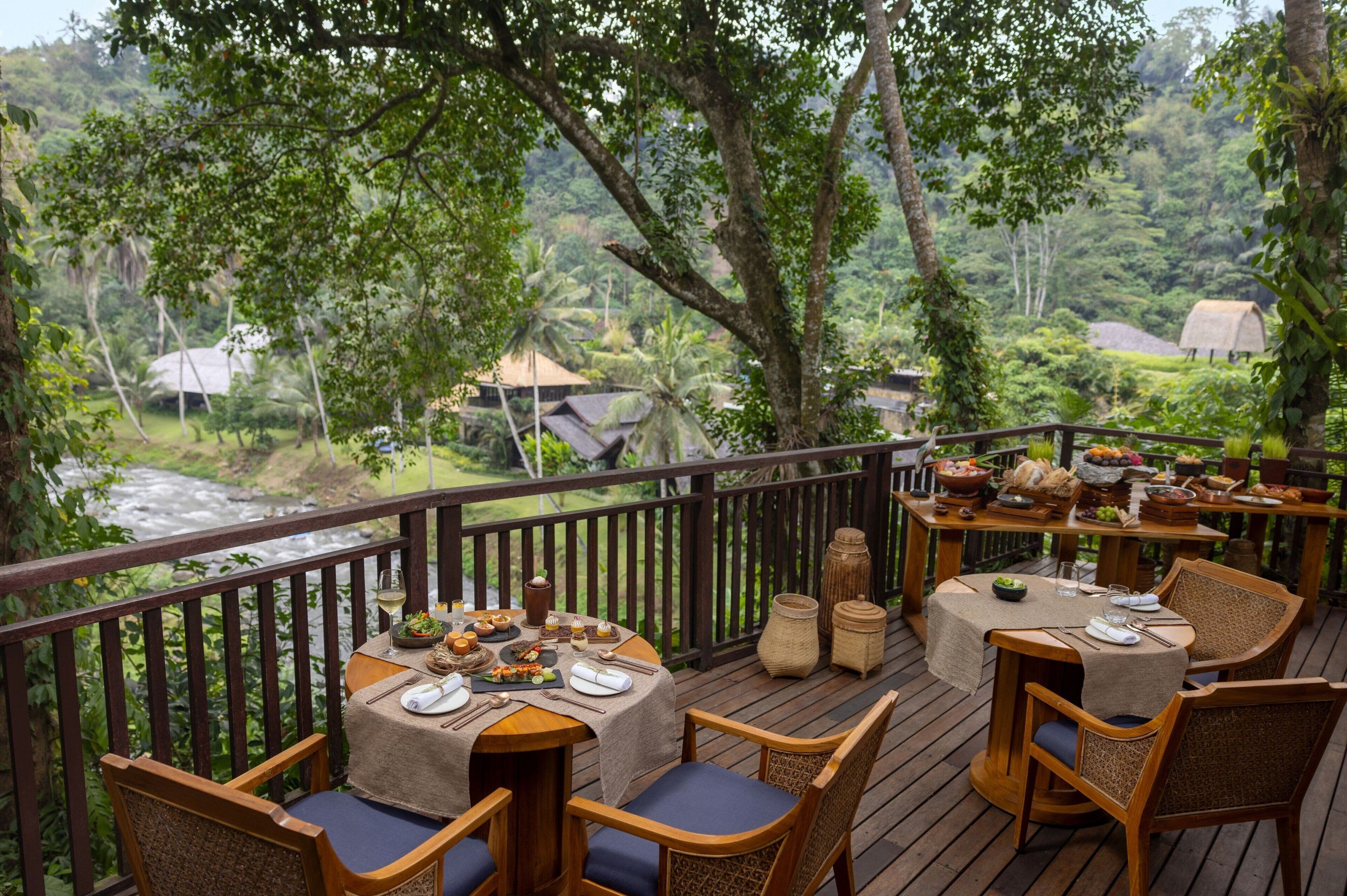 An outdoor dining area with tables set for a meal, overlooking a river and lush greenery.