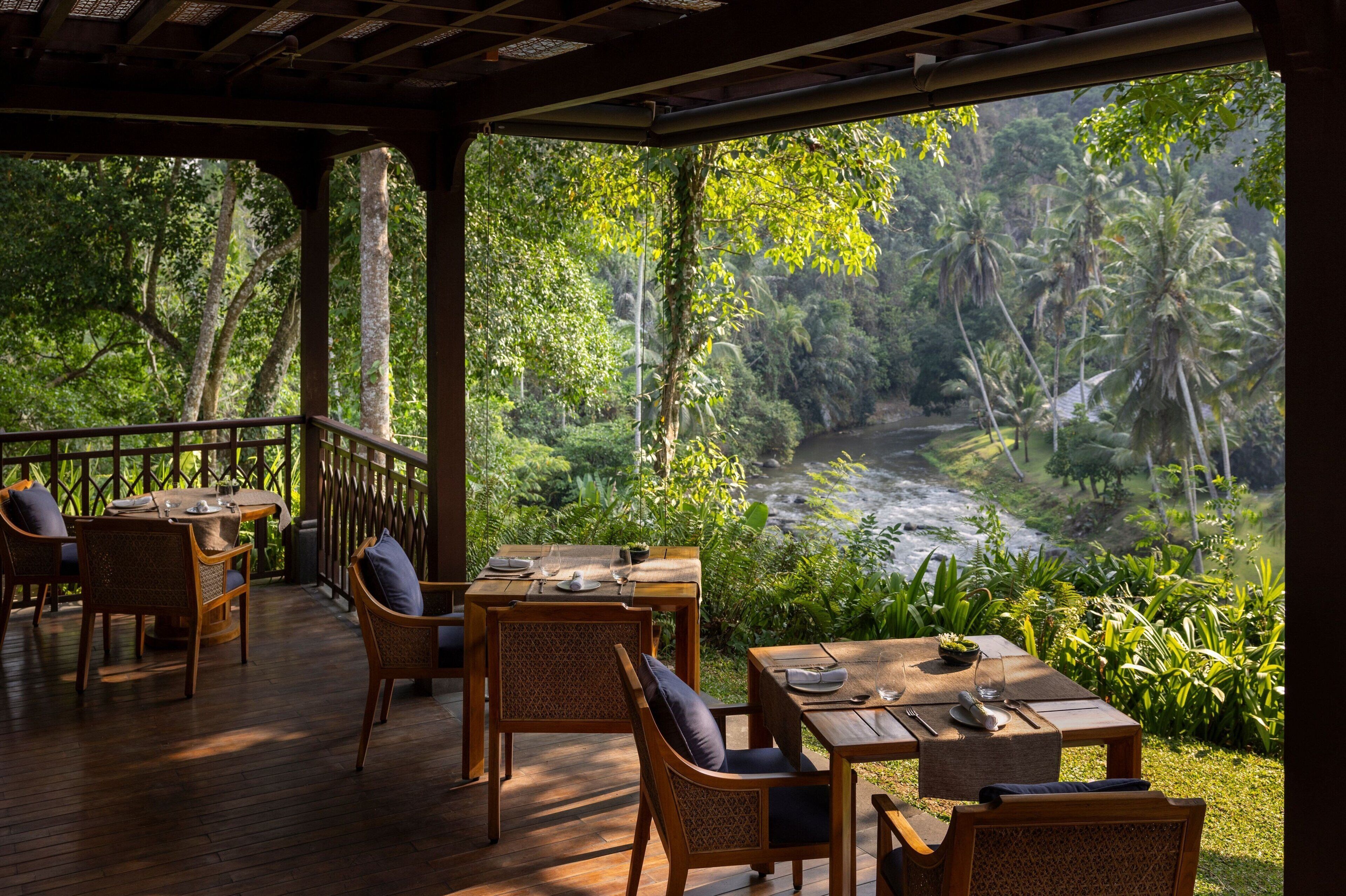 Un espace extérieur abrité, aménagé pour les repas, avec des meubles en bois et une vue sur une rivière et une végétation tropicale.