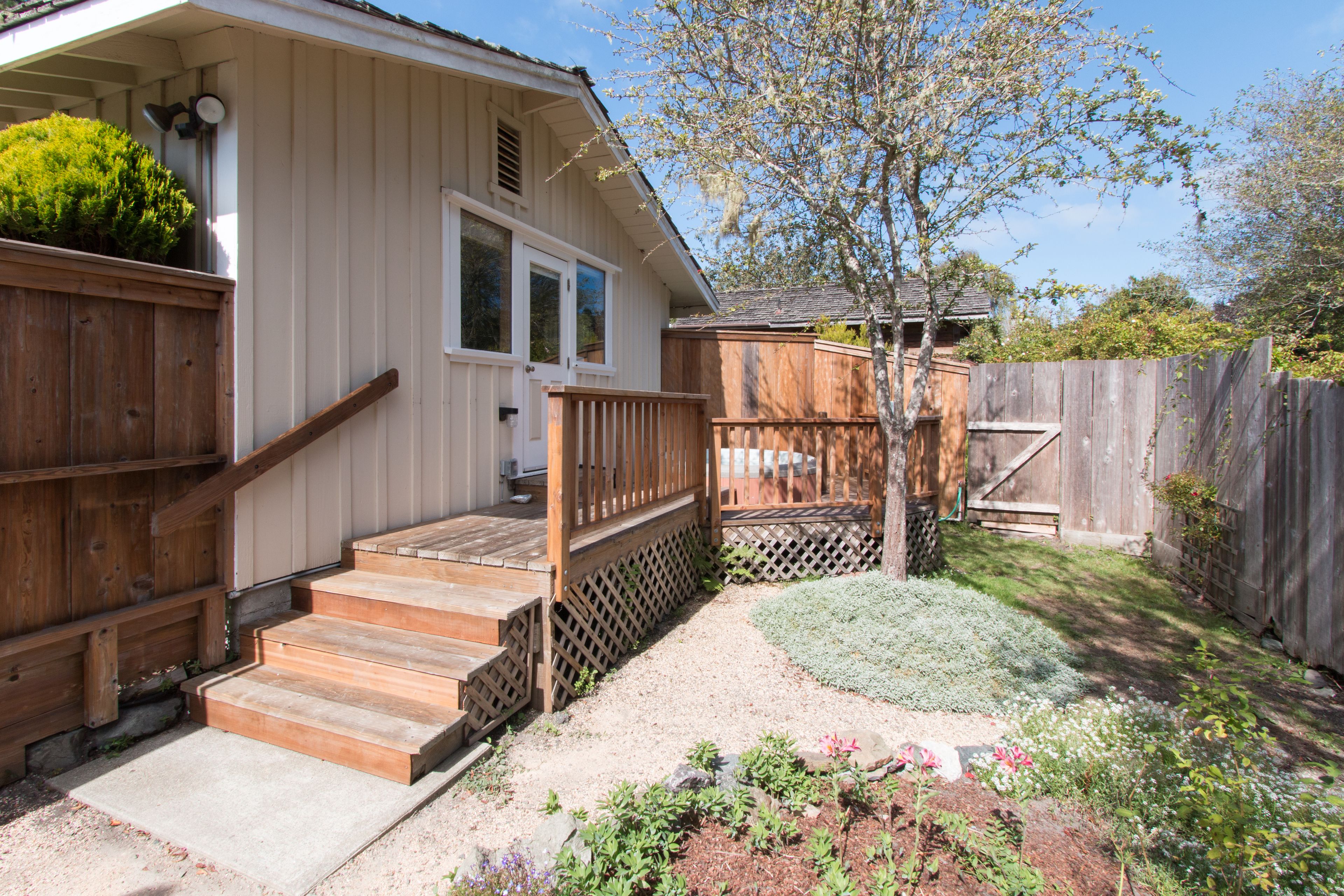 A house with a wooden deck, a front porch, and a garden area with various plants.