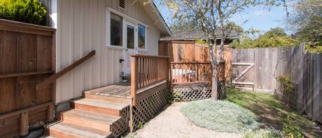 A house with a wooden deck, a front porch, and a garden area with various plants.