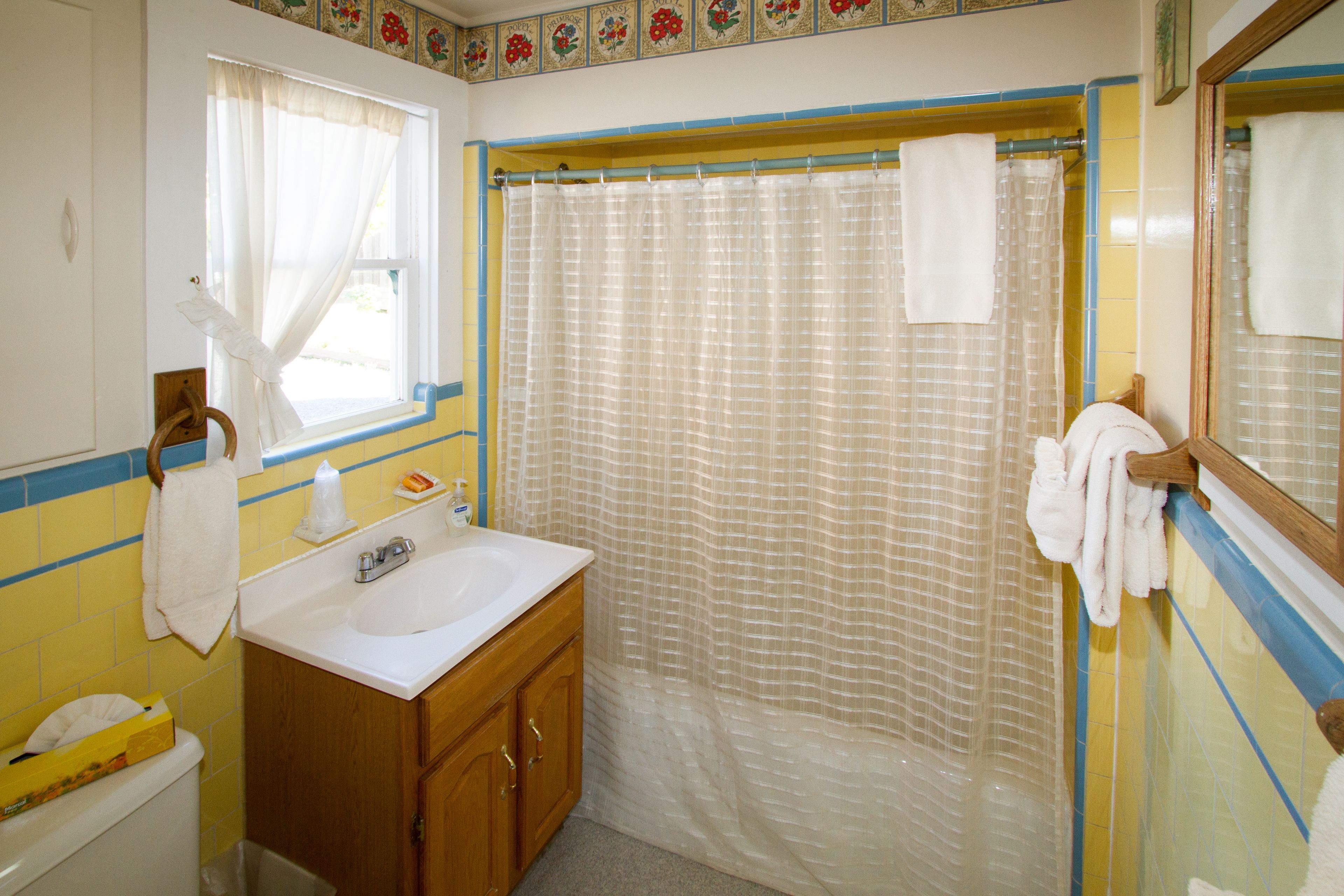 A bathroom with a white sink, wooden cabinets, a shower curtain, and a window with a curtain.