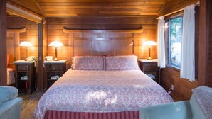 Un dormitorio de cabaña de madera con una cama grande, dos lámparas de noche, un teléfono y una ventana con cortinas.