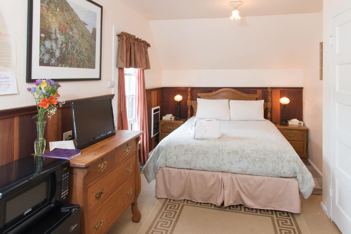 A hotel room with a bed, a TV, a dresser, and a framed picture on the wall.