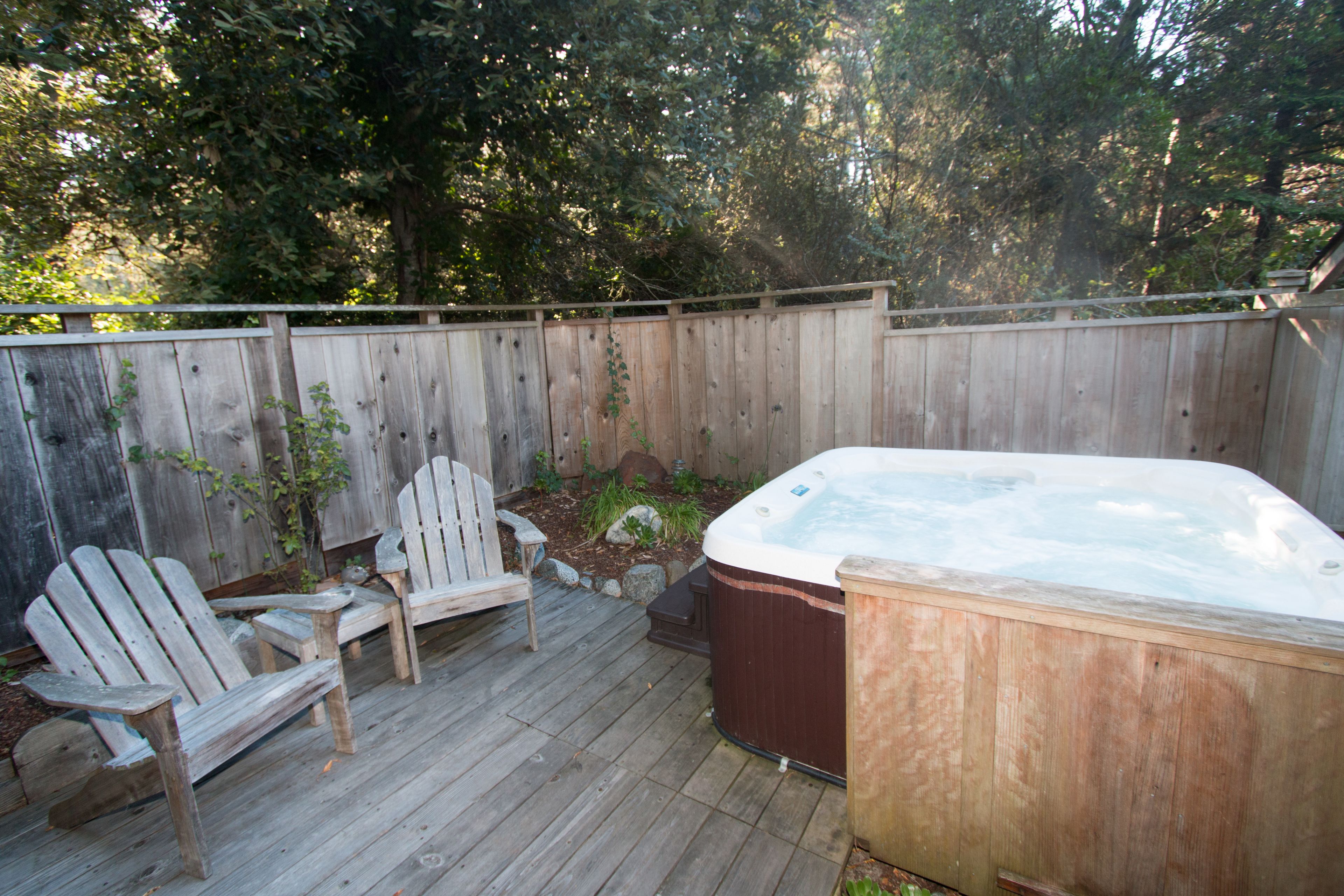 A wooden deck with a hot tub, two Adirondack chairs, and a wooden fence.