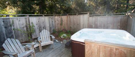 A wooden deck with a hot tub, two Adirondack chairs, and a wooden fence.