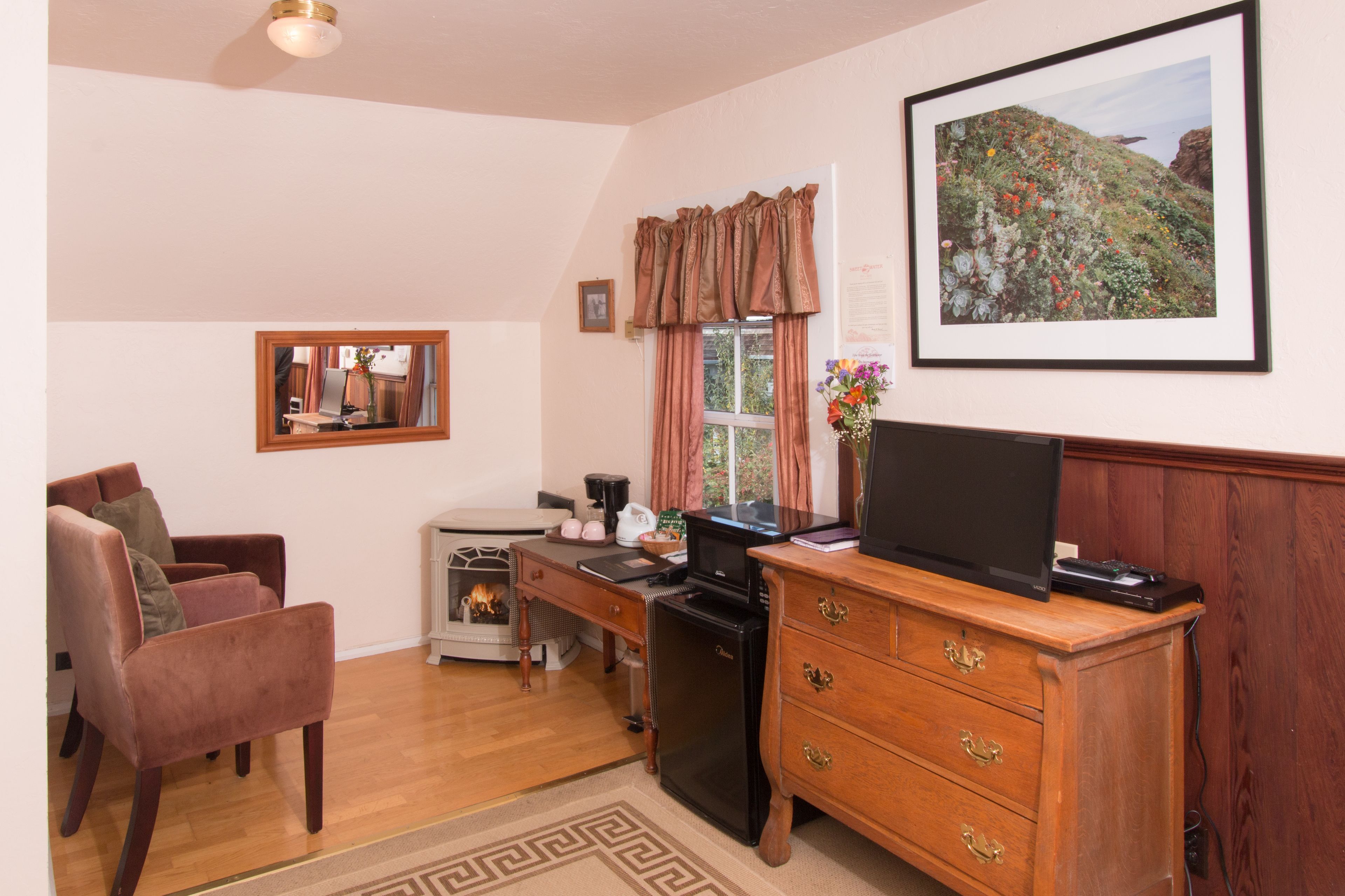 Un salon chaleureux avec une cheminée, un bureau en bois, une télévision et un fauteuil confortable.
