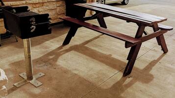 Un patio de concreto con una mesa de picnic de madera y una parrilla.