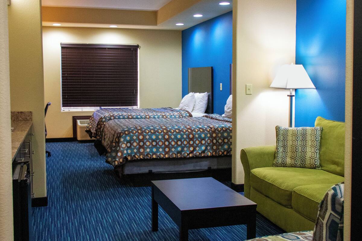 A hotel room with a bed, a green sofa, a small table, and a lamp.