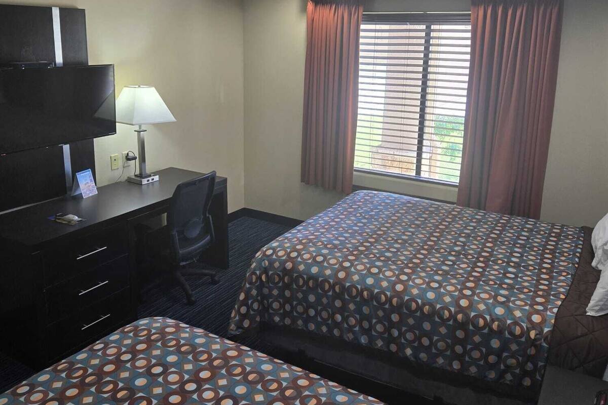 A hotel room with two beds, a desk, a chair, a TV, and a window with curtains.
