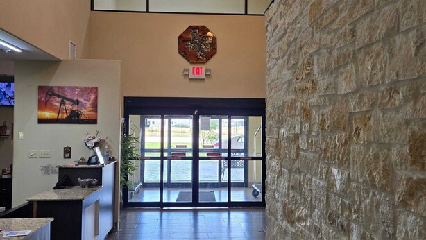 A reception area with a stone wall, a painting of a sunset, and an exit sign. - Karnes City Lodge  (Karnes City)
