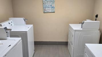 A laundry room with four white washers and dryers, a sign on the wall, and a vent on the right.