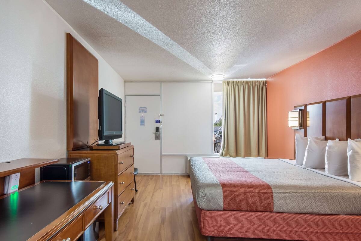 Une chambre d’hôtel comprenant un lit, un bureau avec un ordinateur, une télévision et une porte donnant sur un balcon.