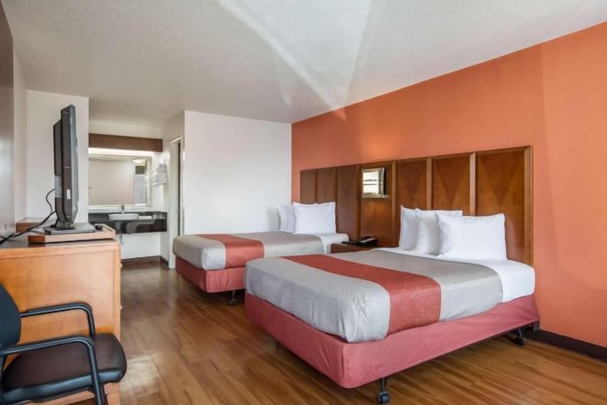 A hotel room with two beds, a desk, and a television.