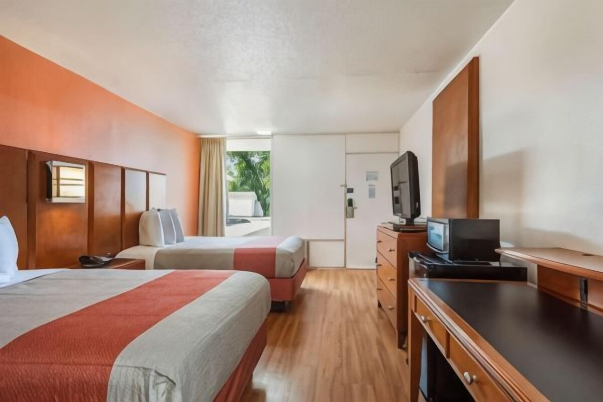Habitación de hotel con dos camas, televisión, escritorio y armario.
