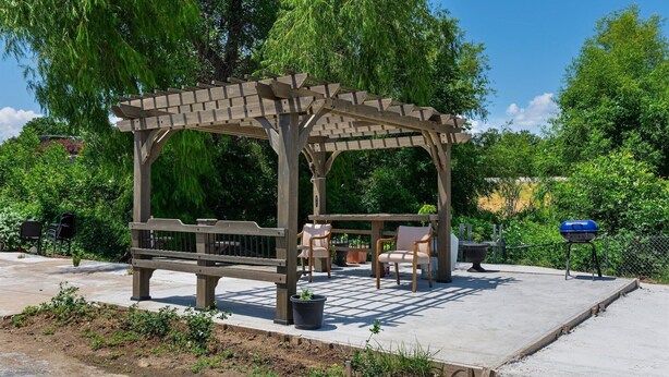 A wooden gazebo with a bench and chairs, surrounded by greenery and a barbecue grill. - Motel 6 Van Buren, AR (Van Buren)