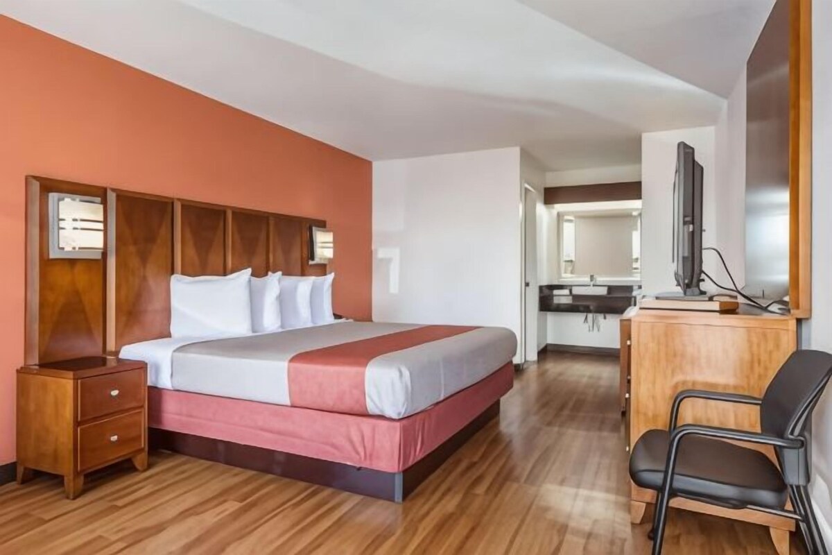 Una habitación de hotel con cama, mesita de noche de madera, escritorio, silla y televisor.
