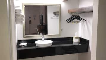 A bathroom with a white sink, black countertop, and a mirror above it. There are towels stacked on the wall and a rack with black hangers.