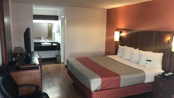 Habitación de hotel con una cama, un escritorio con computadora, una silla y un baño visible a través de una puerta abierta.