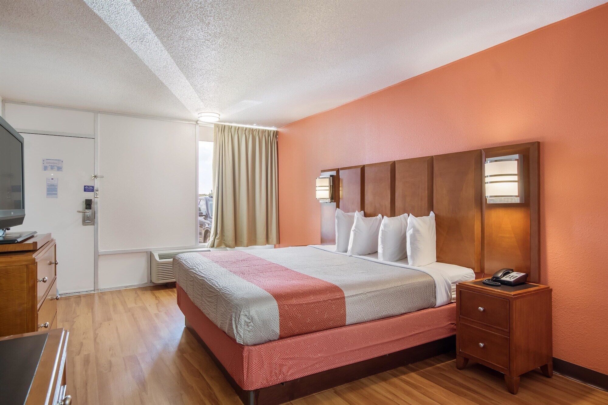 A hotel room with a large bed, a wooden nightstand, a television, and a window with curtains.