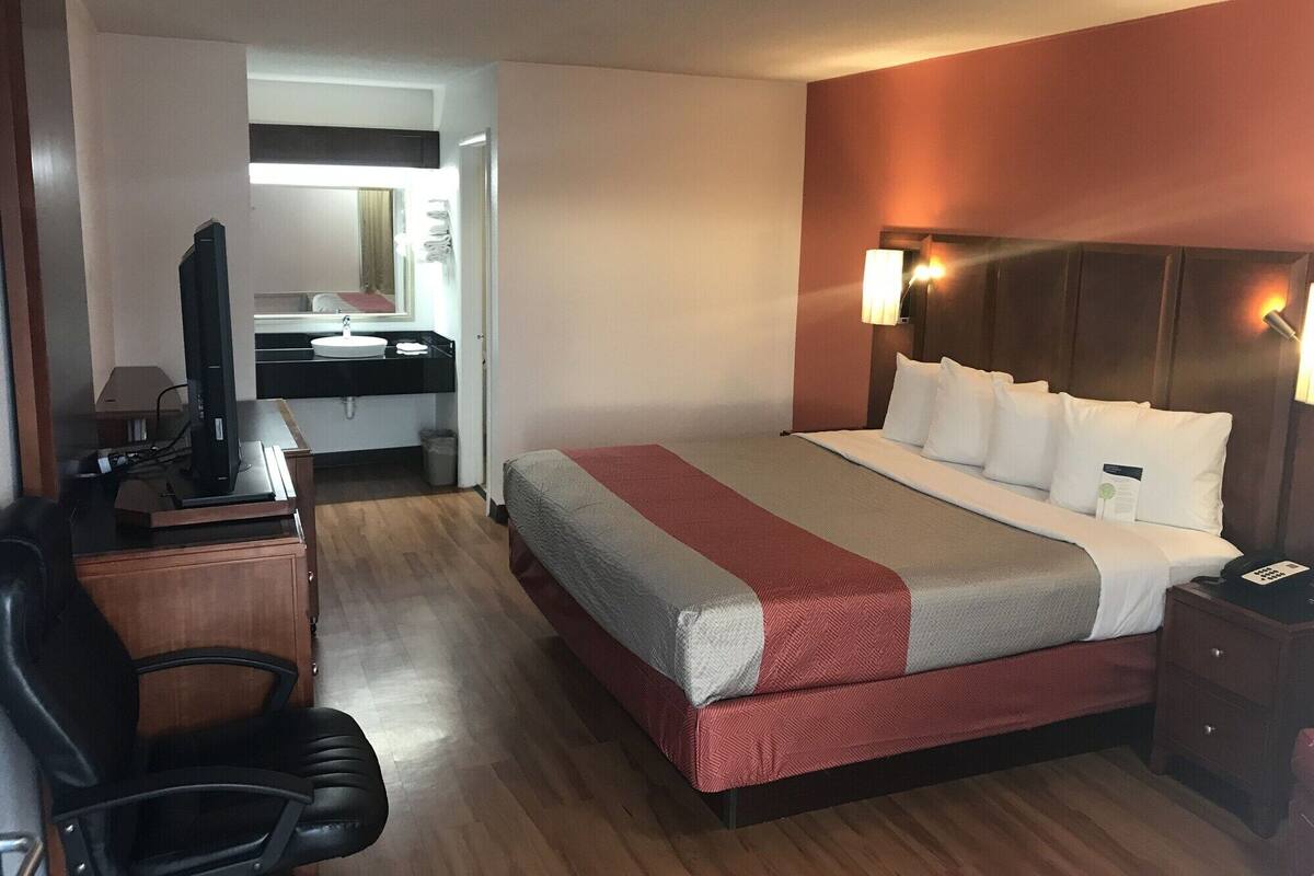 Une chambre d’hôtel comprenant un lit, une table de chevet, une lampe et un bureau avec une télévision.