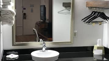 Un baño con un espejo grande, un lavabo redondo, un perchero con toallas dobladas, una encimera negra, un estante de madera con perchas y una botella pequeña sobre la encimera.
