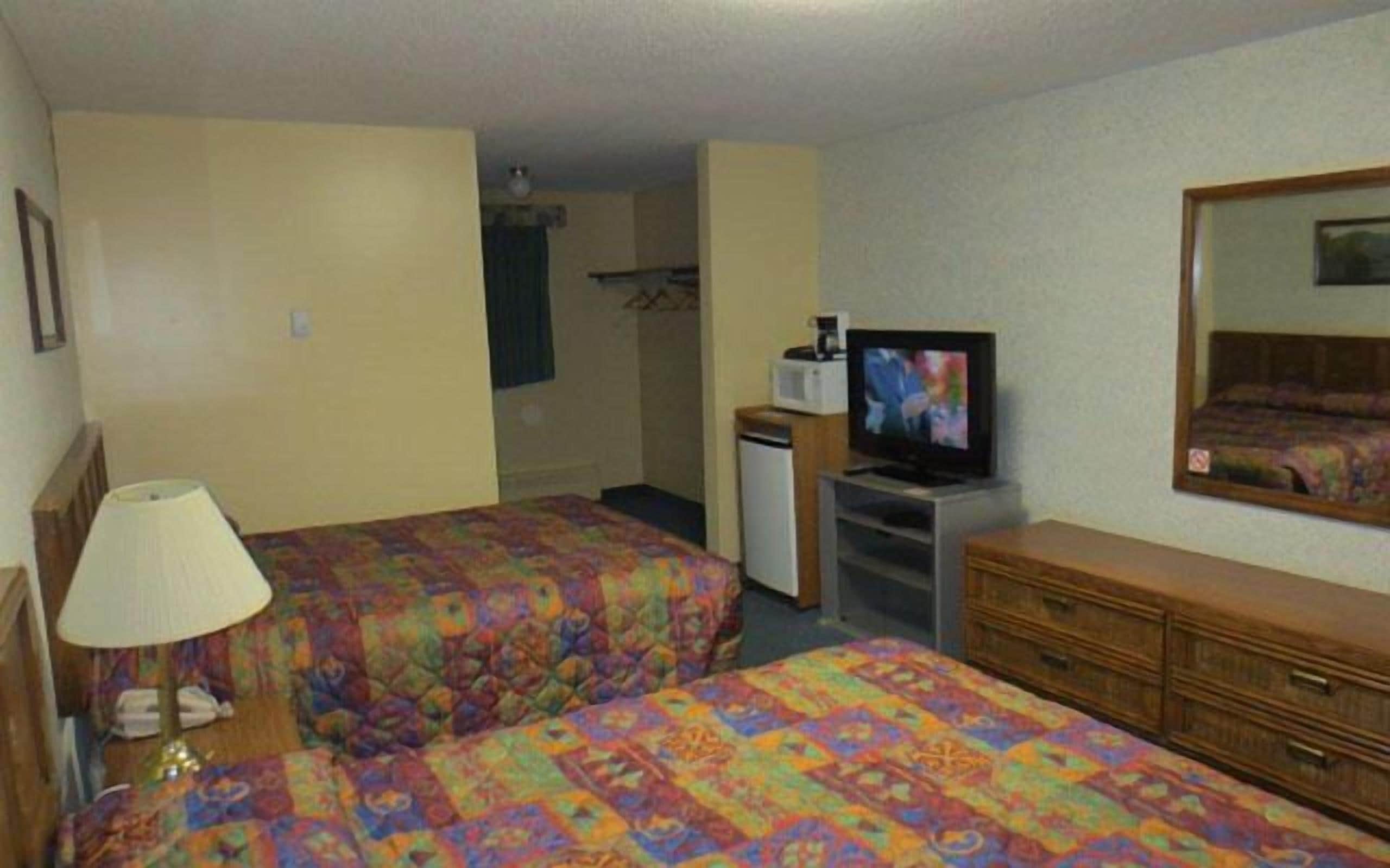 A hotel room with two beds, a TV, a dresser, and a small kitchenette.