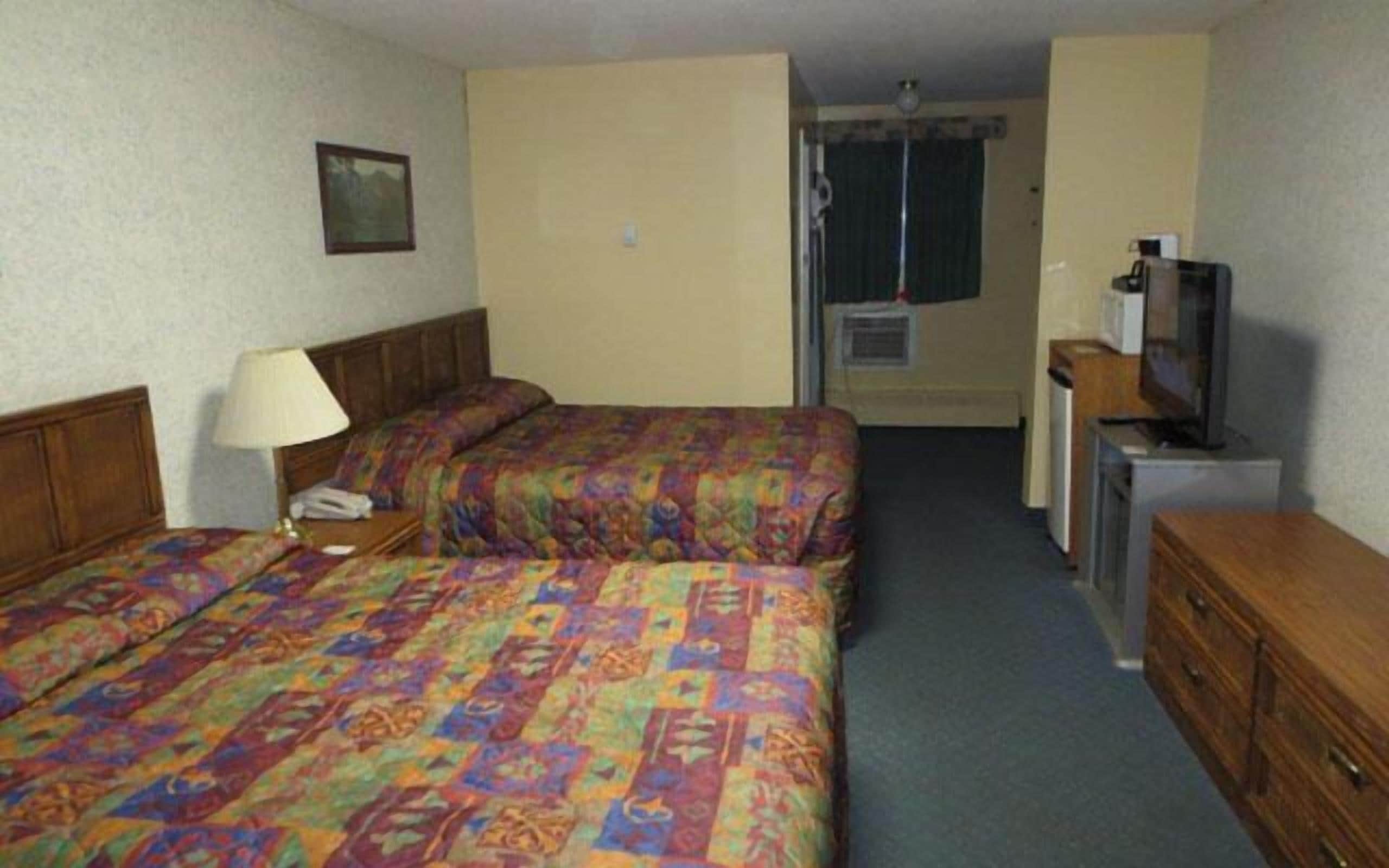 A hotel room with two beds, a desk with a television, a lamp, and a picture on the wall.
