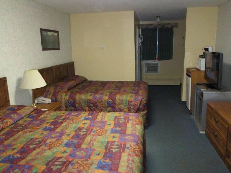 A hotel room with two beds, a desk with a television, a lamp, and a picture on the wall.