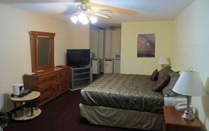 A hotel room with a bed, a television, a dresser, a desk, and a ceiling fan.