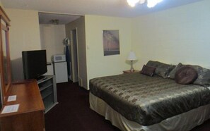A hotel room with a bed, a desk, a television, a microwave, and a door leading to another room.