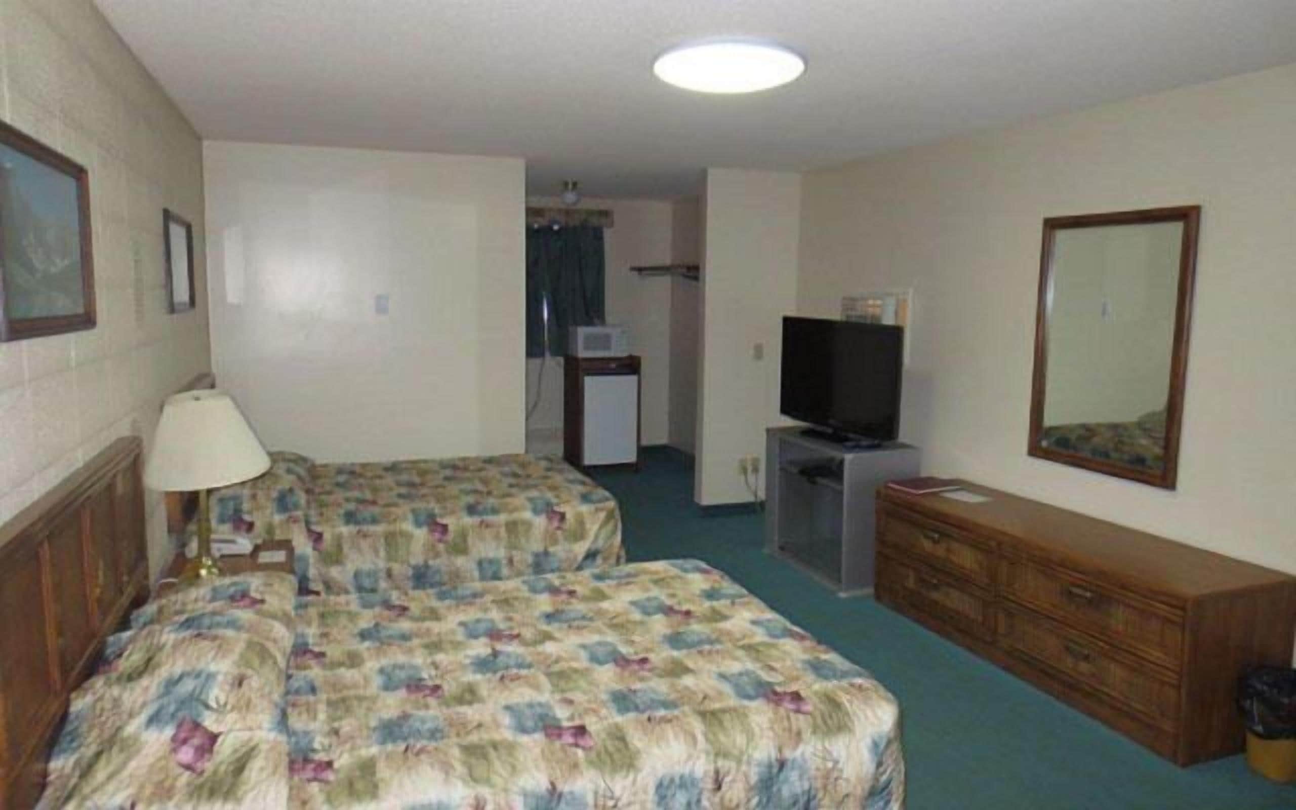 A hotel room with two beds, a dresser, a television, and a small kitchenette.