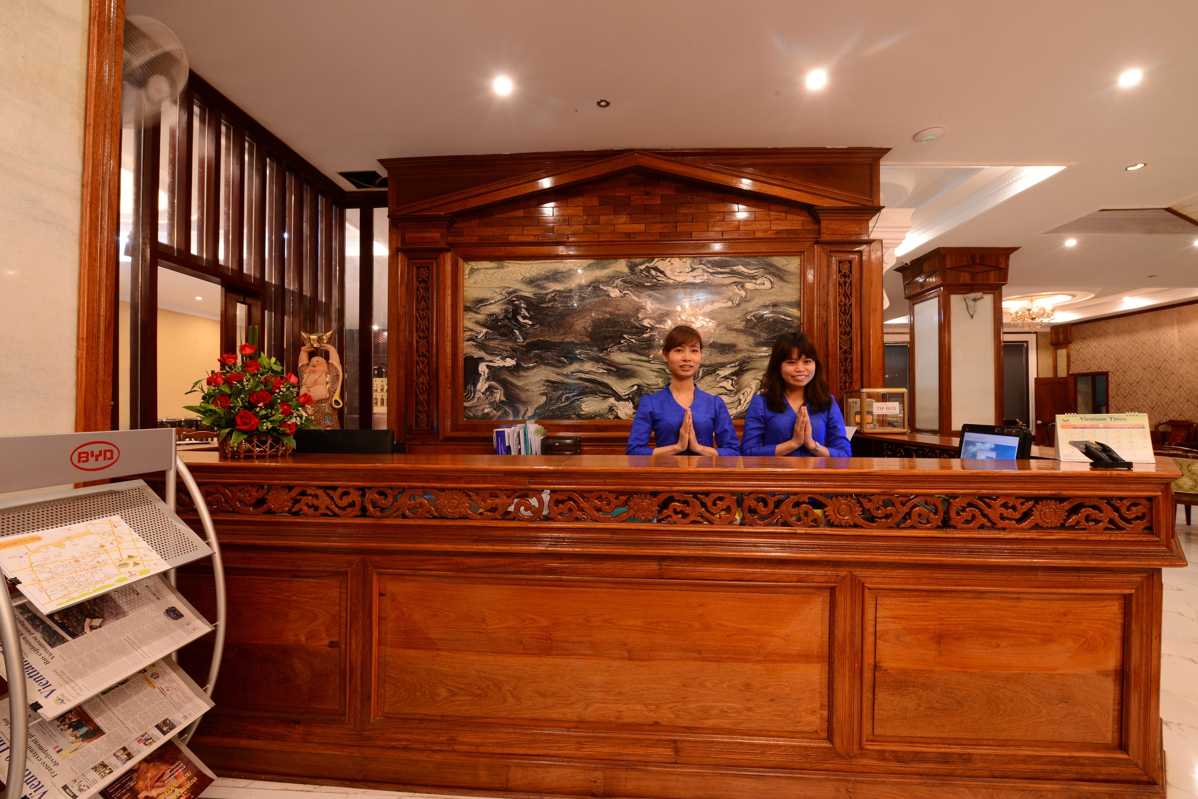 A reception desk with two staff members, a wooden panel design, a large mural, and a BYD self-service kiosk.
