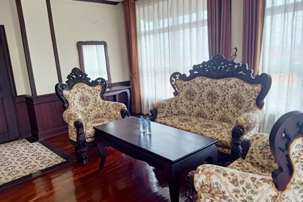 A room with a patterned sofa and armchairs, a wooden coffee table, and a mirror on the wall.