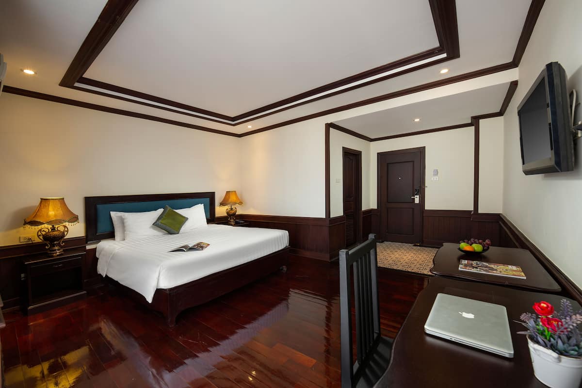 Une chambre d’hôtel avec un grand lit, un plancher en bois, un bureau avec un ordinateur portable, une télévision et un panier de fruits.