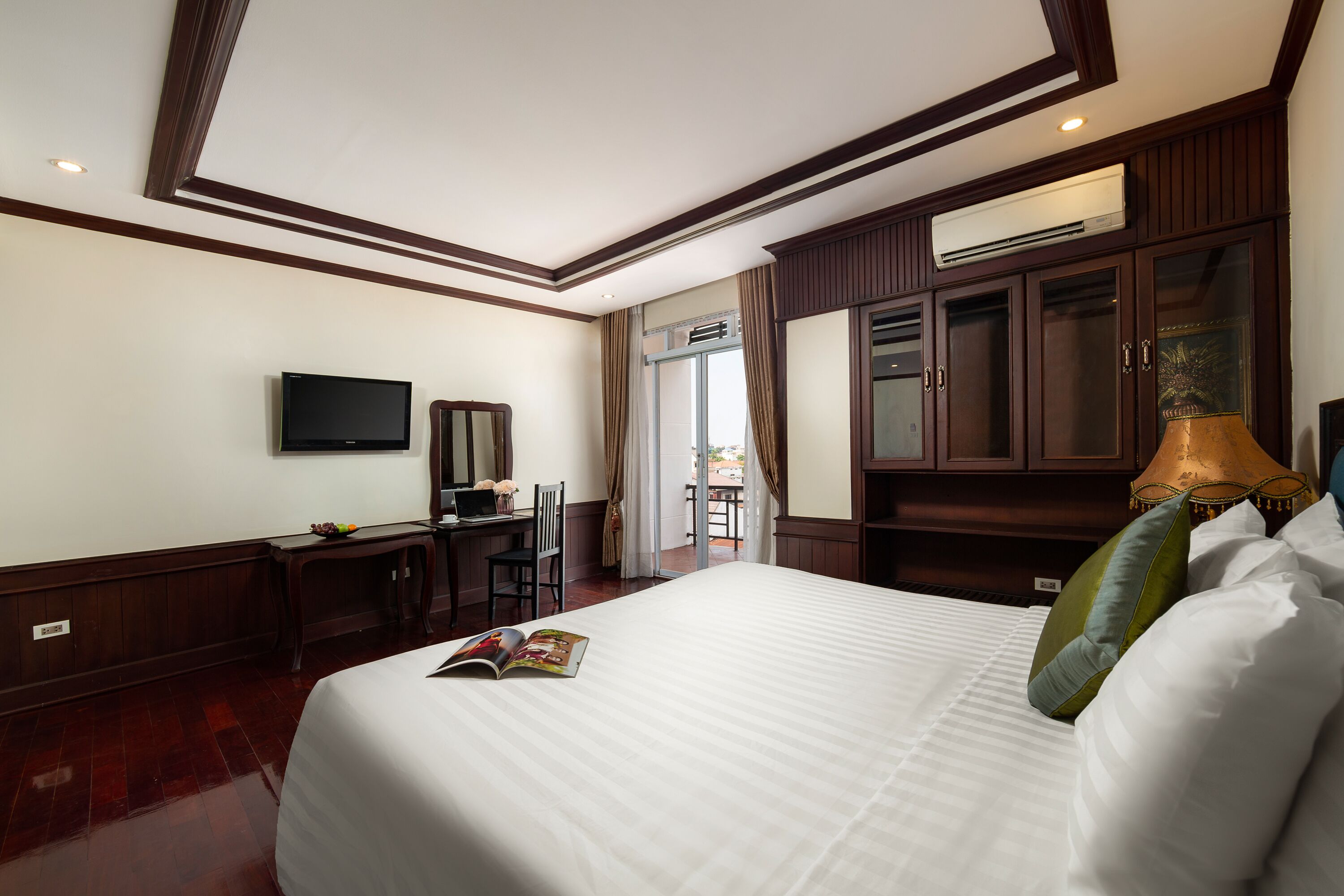 A hotel room with a large bed, a desk with a computer, a television, and a wardrobe.