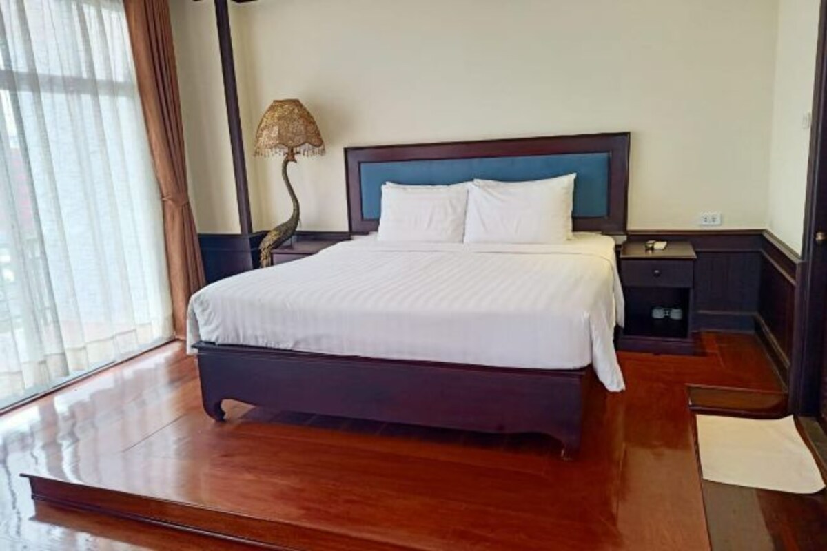 A hotel room with a large bed, a nightstand, a lamp, and a window with curtains.